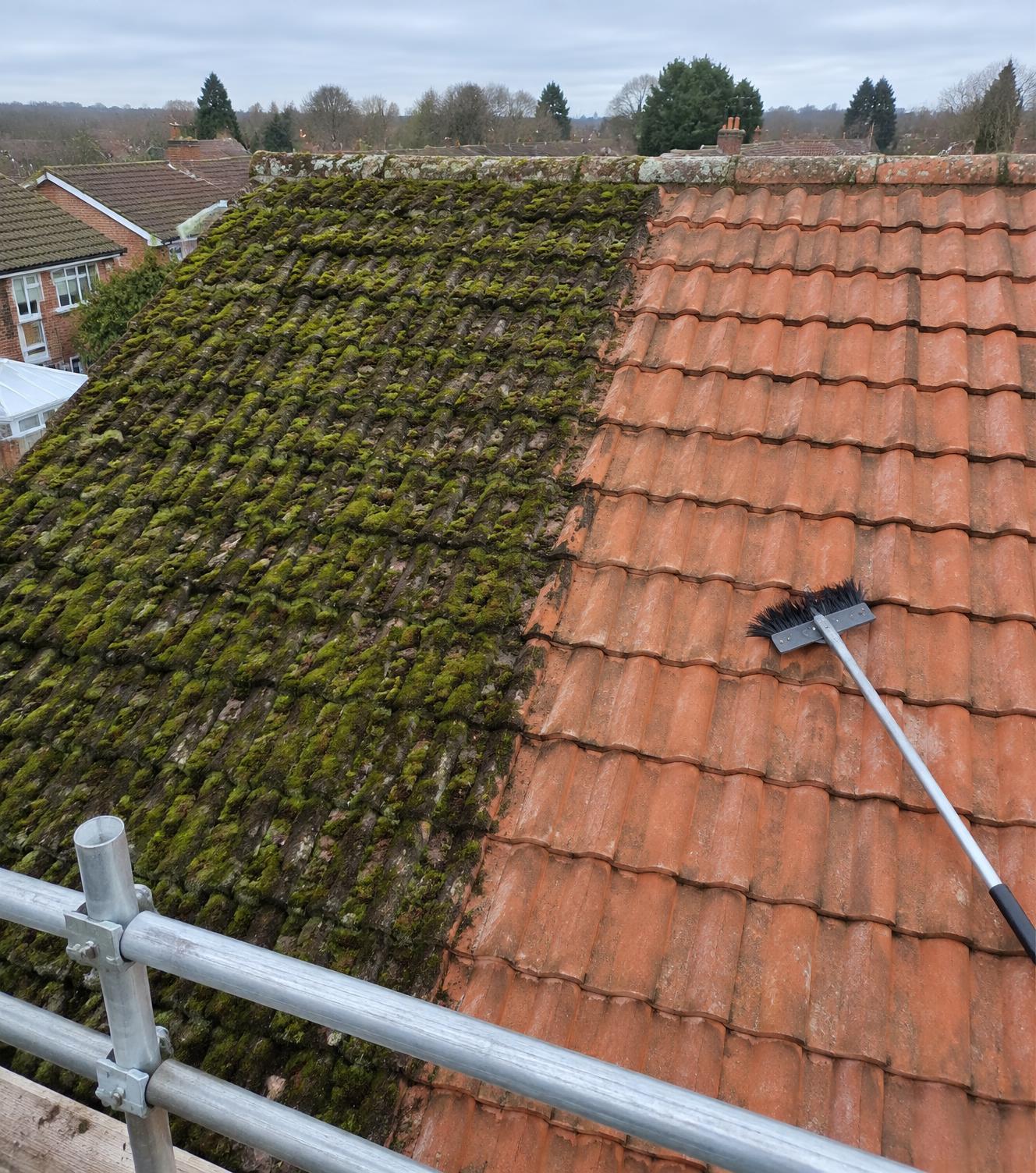 Clay tiled roof being cleaned by hand, half the slope still covered in moss and the other half freshly scraped clean